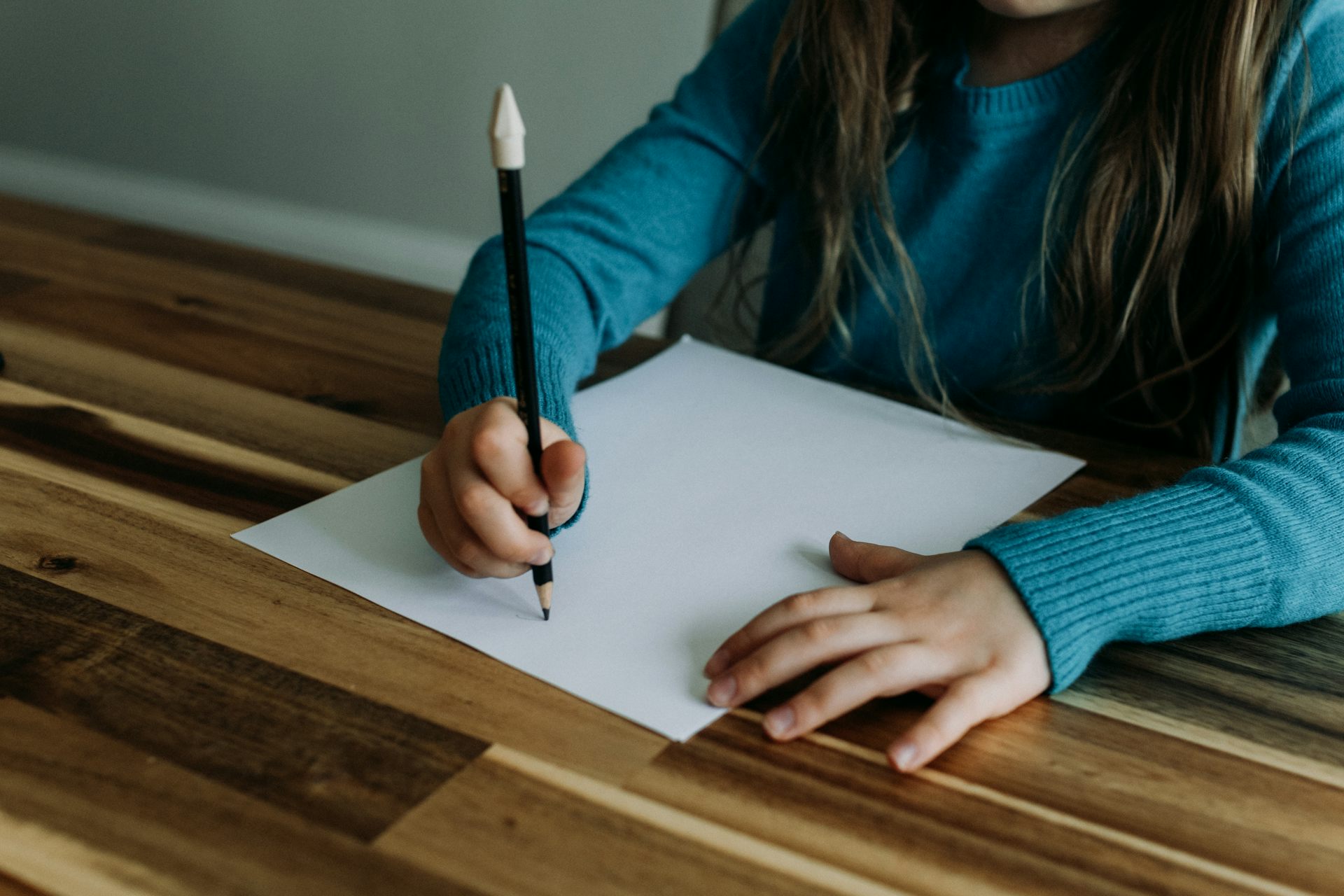 A student writing with a pencil at a wooden desk